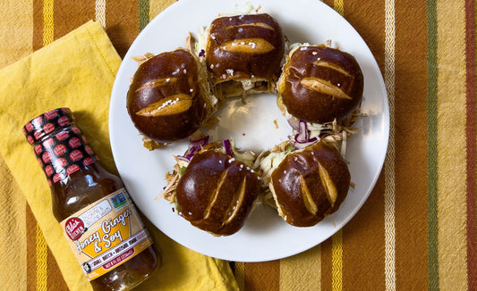 Pretzel bun pulled pork sliders with a bottle of Elda's Kitchen Honey Ginger & Soy sauce.