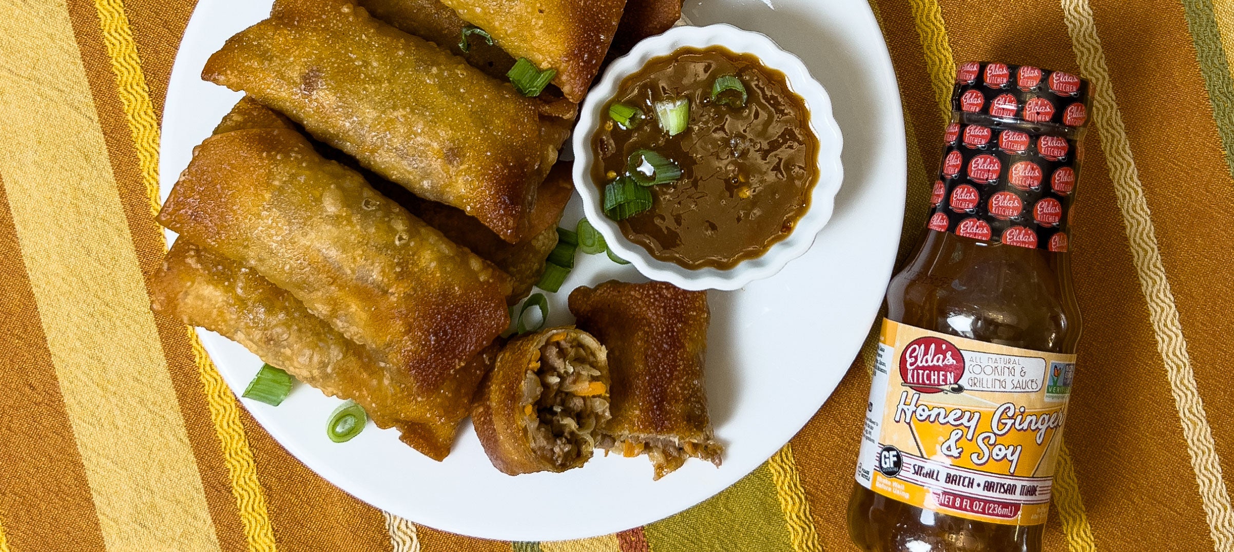 Fried egg rolls with a bottle of Elda's Kitchen Honey Ginger & Soy Sauce