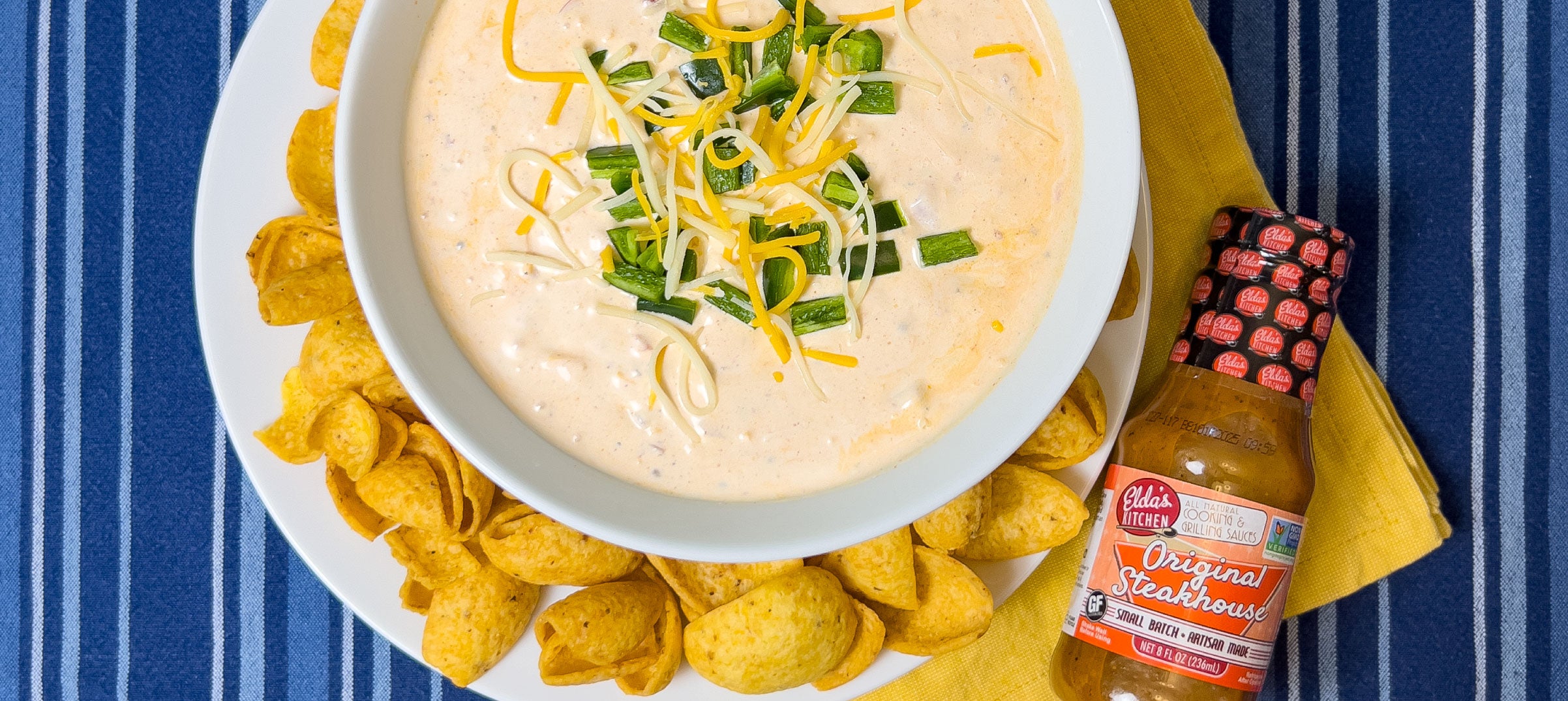Creamy dip with chips and a bottle of Elda's Kitchen Original Steakhouse Sauce.