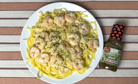 Plate of shrimp fettuccine pasta with shrimp next to a bottle of Elda's Kitchen Garlic and Herb Sauce.