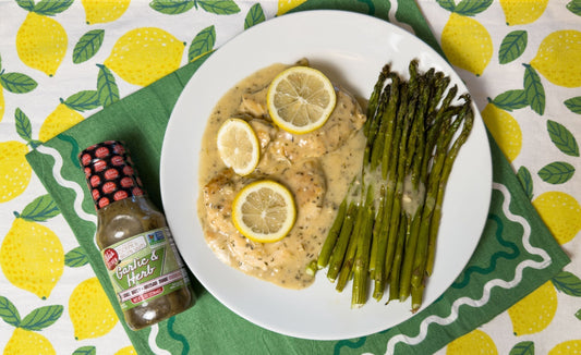 Plate of lemon garlic chicken and asparagus with a bottle of Elda's Kitchen Garlic & Herb Sauce.