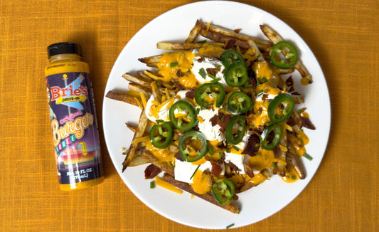 Plate of loaded french fries with sour cream and fresh jalapenos next to a bottle of Brie's Drive-In Burger Sauce.