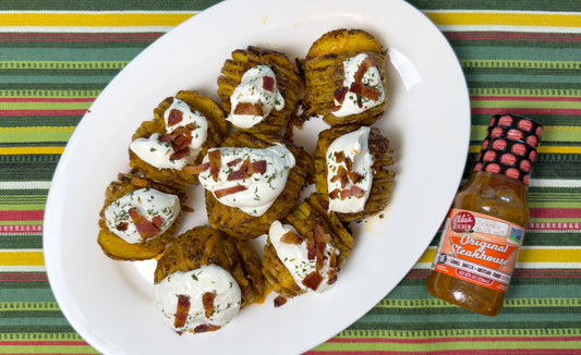 Plate of sliced, loaded baked potatoes topped with sourcream and bacon next to a bottle of Elda's Kitchen Original Steakhouse Sauce