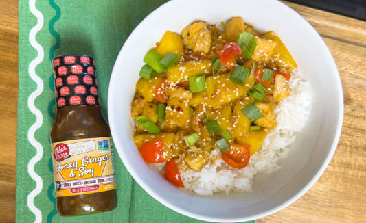 A bowl with rice, chicken, pineapple next to a bottle of Elda's Kitchen Honey Ginger & Soy Sauce.