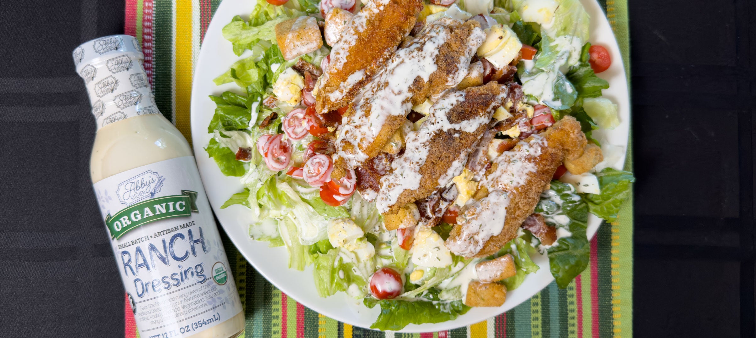 Salad with fried chicken, egg, tomatoes, and lettuce next to a bottle of Abby's Kitchen Organic Ranch Dressing