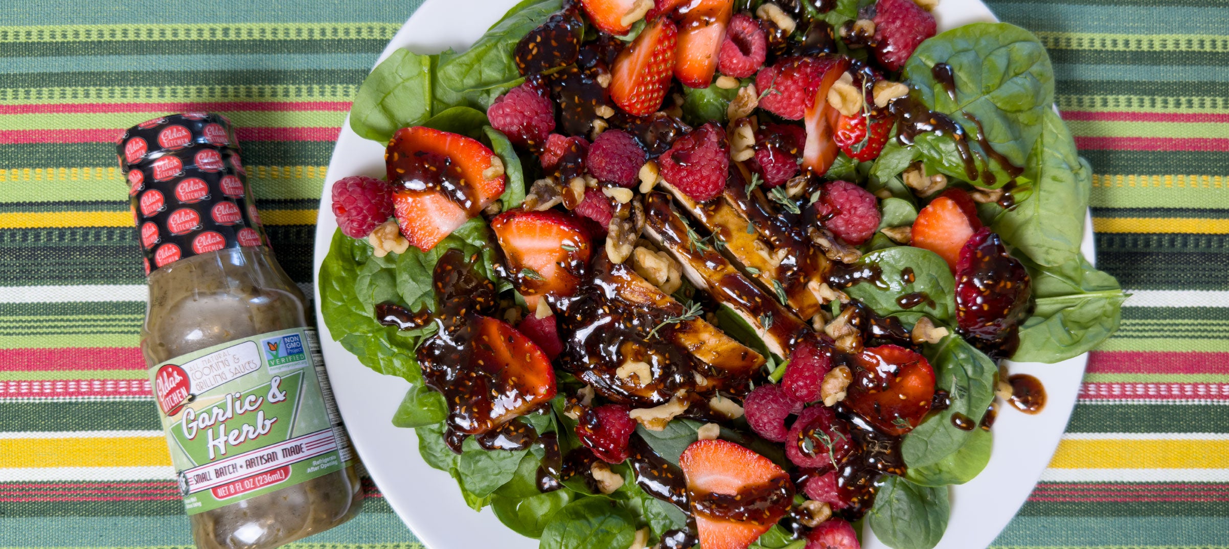Salad with strawberries, raspberries, and nuts with Elda's Kitchen Garlic & Herb Sauce bottle
