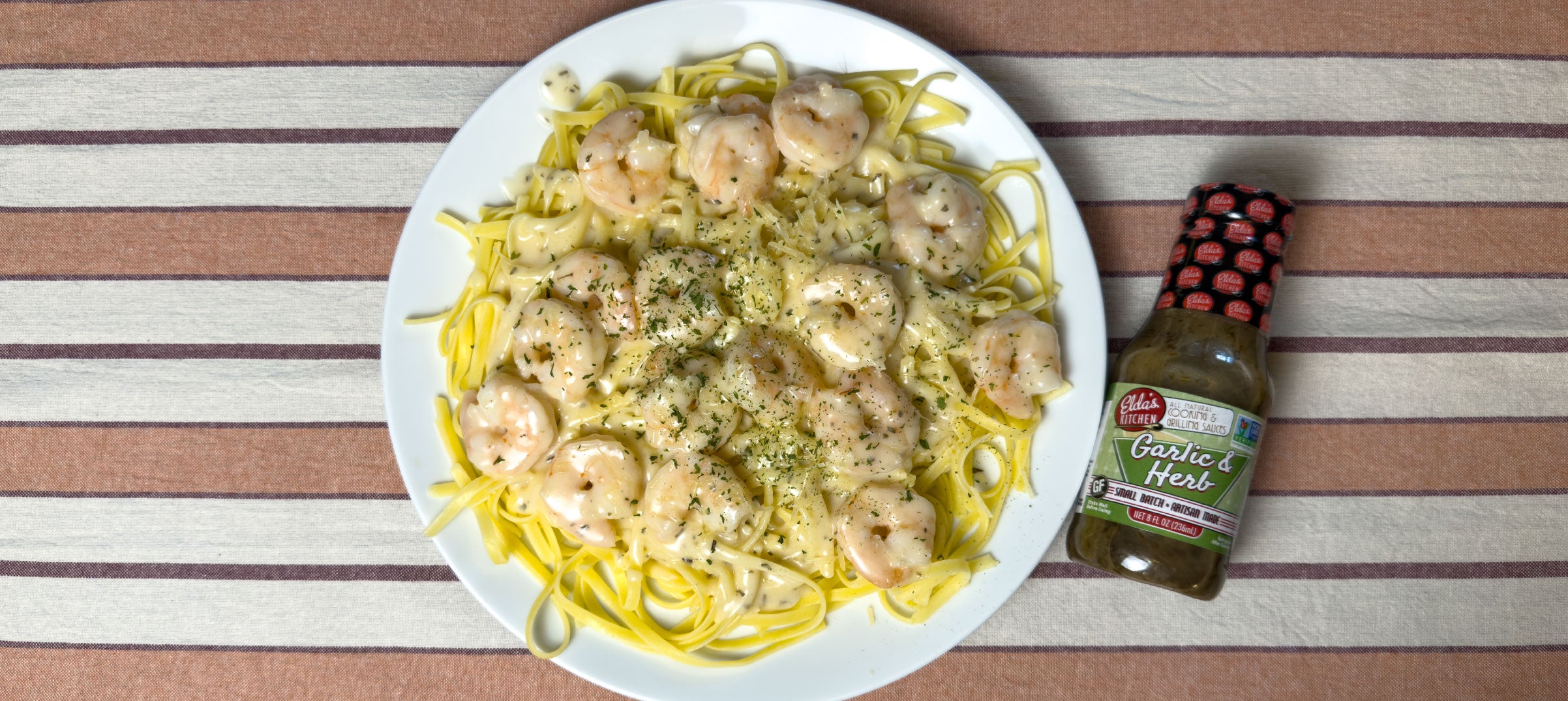 Plate of shrimp fettuccine pasta with shrimp next to a bottle of Elda's Kitchen Garlic and Herb Sauce.